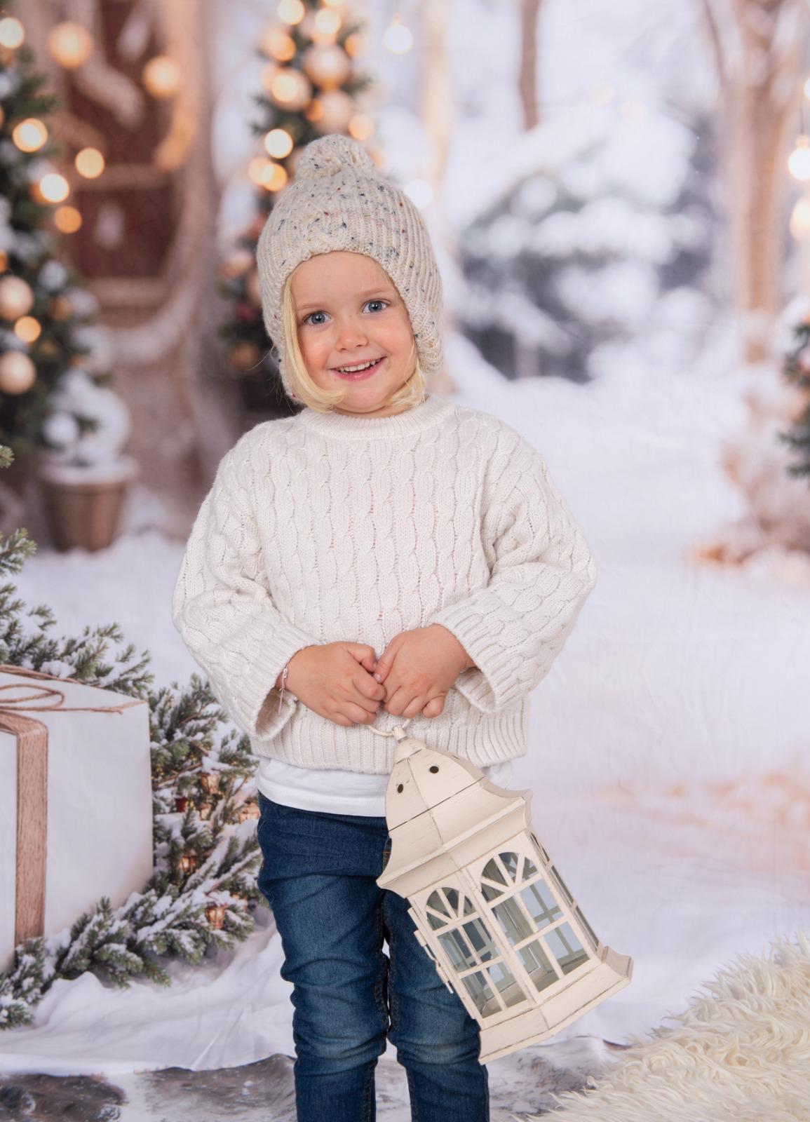 Mädchen mit Strickmütze und Laterne vor verschneiten Christbäumen